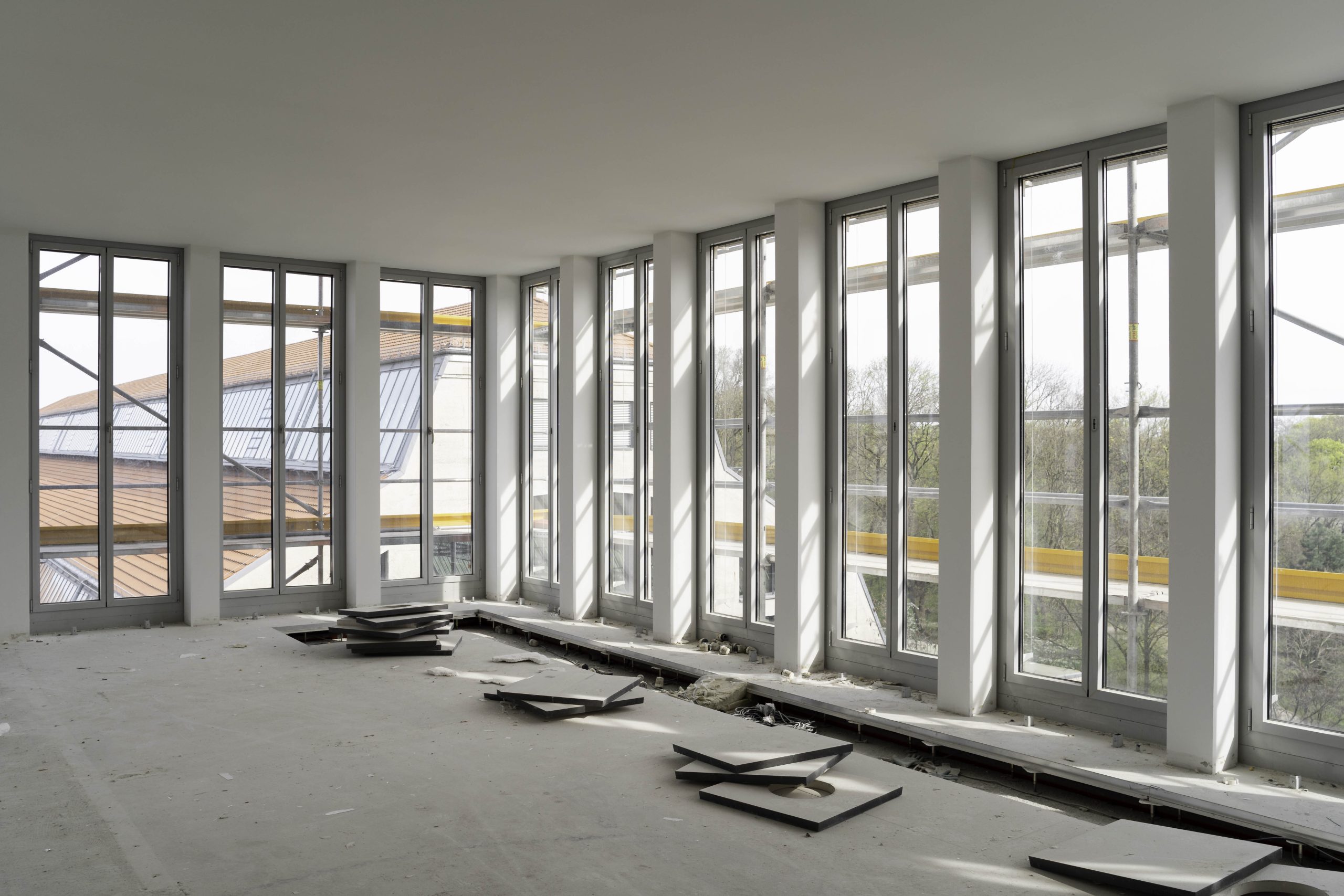 Heller, leerstehender Raum mit großen bodentiefen Fenstern. Im Raum liegen entfernte Bodenpaletten.
