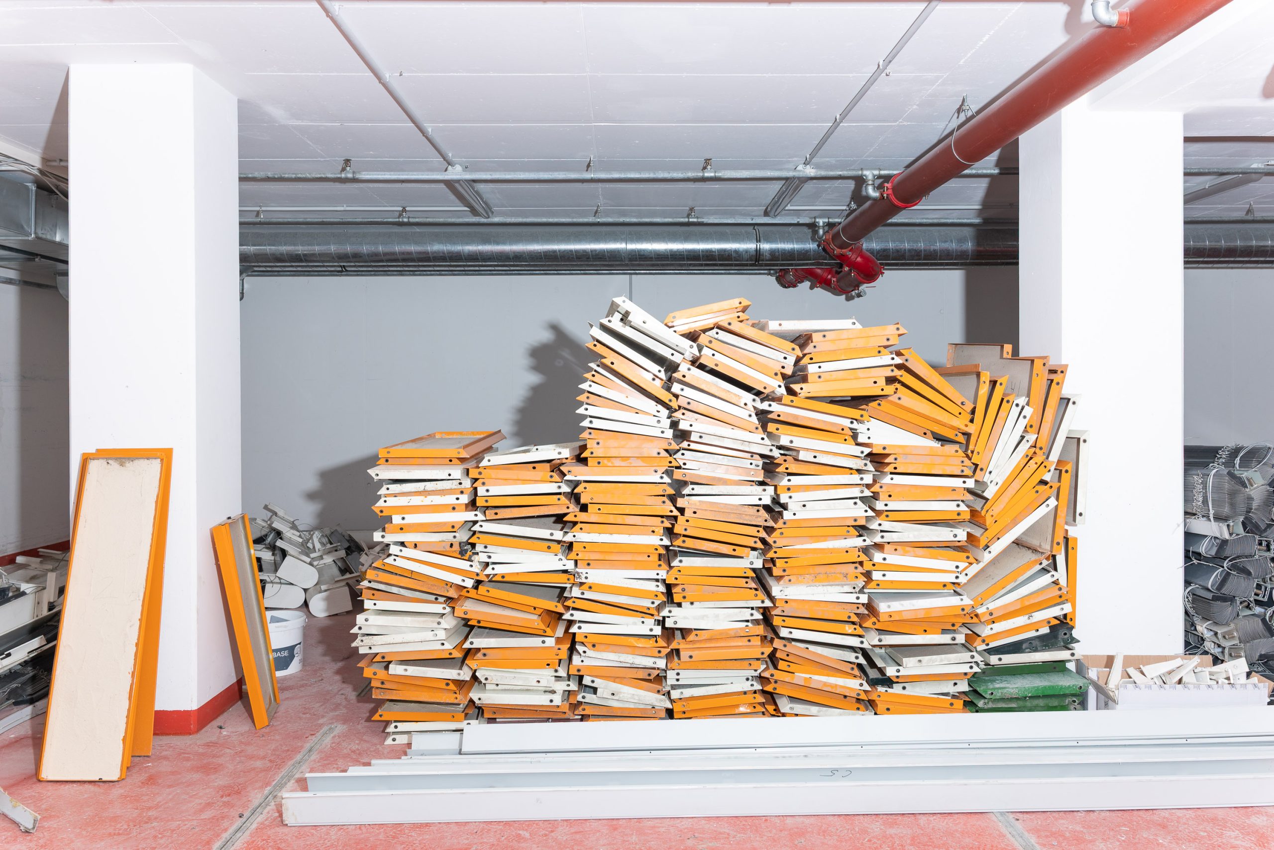 In einem Innenraum liegt ein großer Stapel orange-weißer, rechteckiger Bauteile gestapelt nebeneinander.