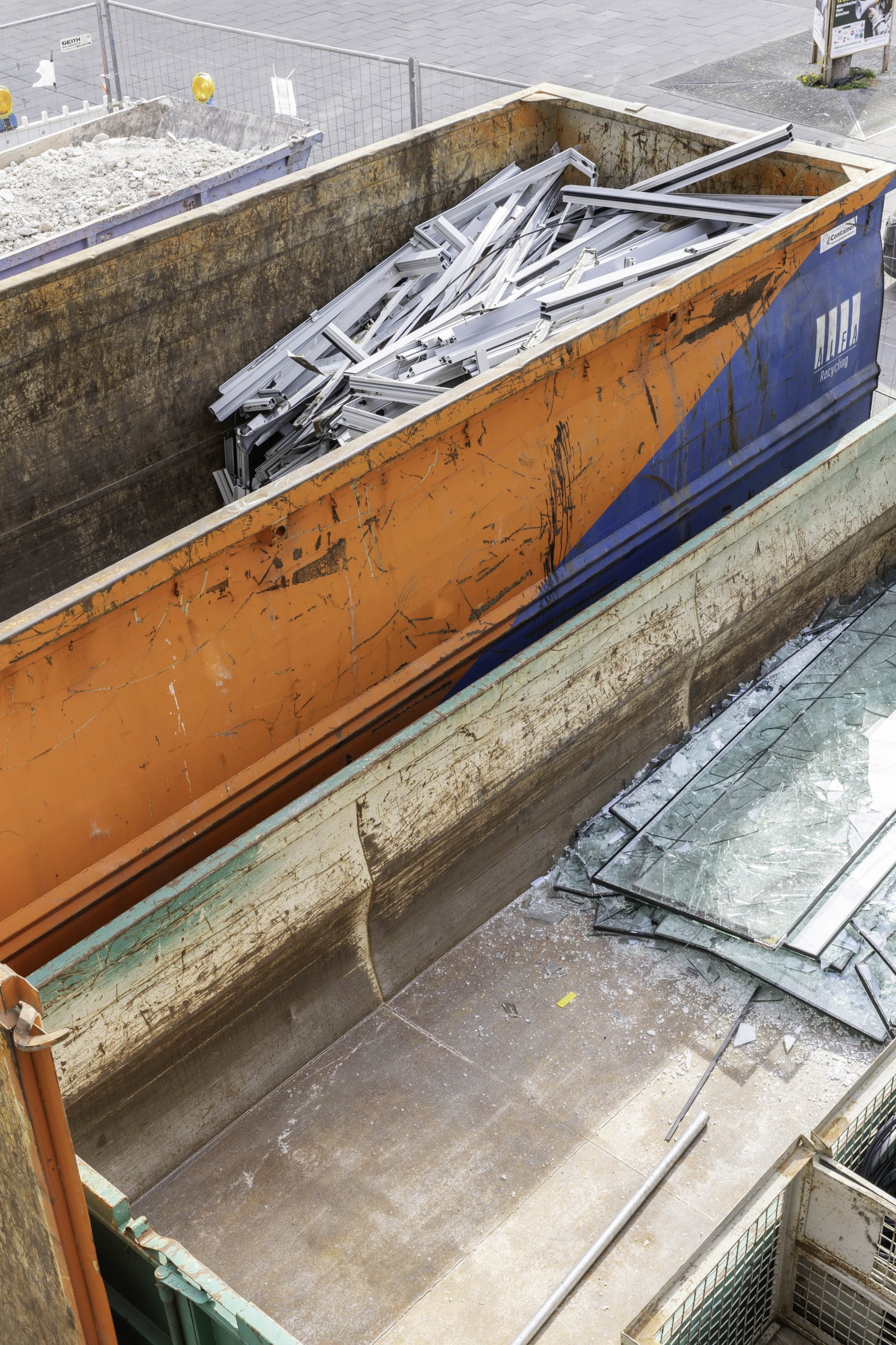 Ein großer Container gefüllt mit ausgebauten Fensterrahmen. Direkt davor liegen kaputte Glasscheiben